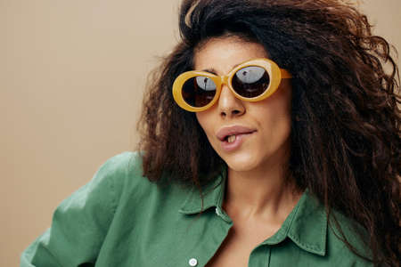 FASHION CONCEPT. Fabulous tanned curly Latin female in casual things sunglasses curl of lip posing...