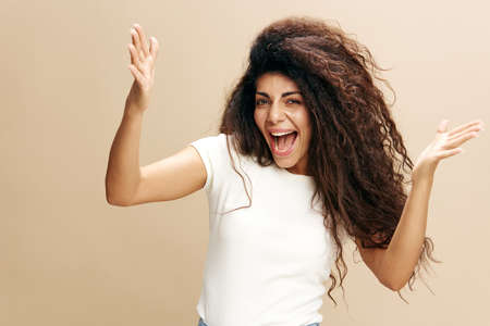 Happy joyful young Latin woman in casual gray sweatshirt doing winner gesture celebrating clenching...