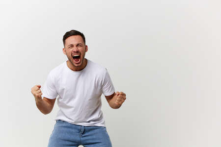 Screaming angry aggressive crazy tanned handsome man in basic t-shirt clenches his fists posing...