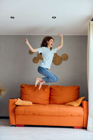 cheerful woman jumping on the couch at home entertainmentの写真素材