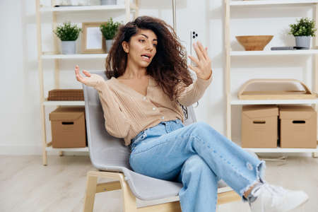 Overjoyed angry irritated tanned curly Latin lady have video call hold trendy smartphone sit on...