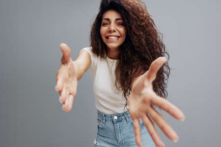 Come To Me. Excited Latin Lady Extending Hands At Camera, Holding Big Invisible Object, Curly Woman Offering Hugs Or Wants To Grab Something, Standing Isolated Over Gray Background, Copy Spaceの写真素材