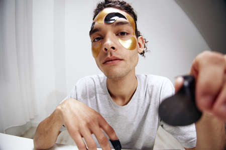 A young man in a white T-shirt with patches on the face rejuvenation skin care