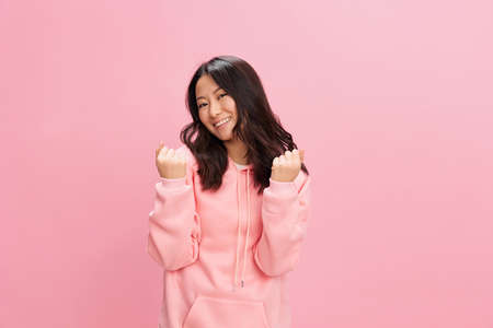 Overjoyed happy Asian student young lady in pink hoodie sweatshirt point fists up posing isolated on over pink studio background. Good offer. Fashion New Collection concept. Copy spaceの写真素材