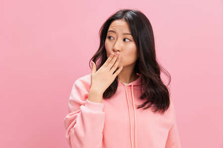 Adorable lovely Asian student young lady in pink hoodie sweatshirt sends kiss to you posing isolated on over pink studio background. Good offer. Fashion New Collection concept. Copy spaceの写真素材