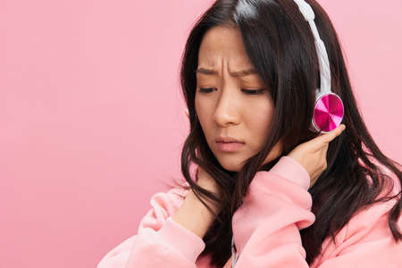 Upset confused Asian student young lady in pink hoodie sweatshirt with cute headphones looks at you posing isolated on over pink studio background. Good offer. Sound streaming platform ad conceptの写真素材