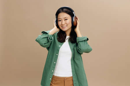 Enjoy this sound. Happy cute Asian student young woman in khaki green shirt touch headphones posing...