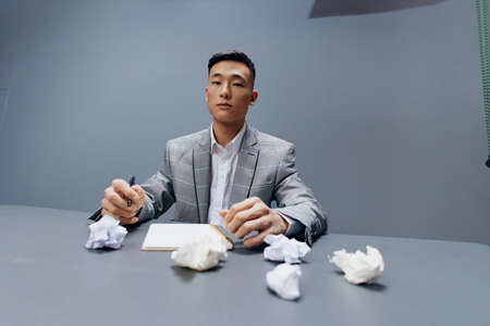 businessmen in a suit sits at a table emotions crumpled paper Gray backgroundの写真素材