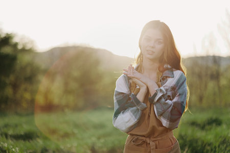 Portrait of a young smiling woman in work clothes checkered shirt and apron in nature in the evening...