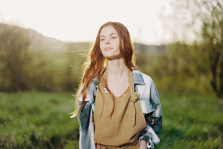 Portrait of a young smiling woman in work clothes checkered shirt and apron in nature in the evening after workの写真素材