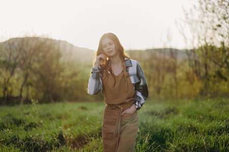 Portrait of a young smiling woman in work clothes checkered shirt and apron in nature in the evening...
