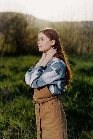 Portrait of a young smiling woman in work clothes checkered shirt and apron in nature in the evening...
