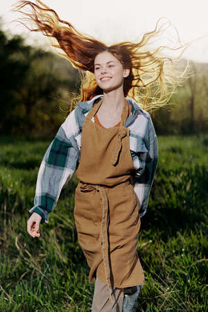 Woman walking on the grass in nature smiling in farm clothes with beautiful hair flying in the wind...