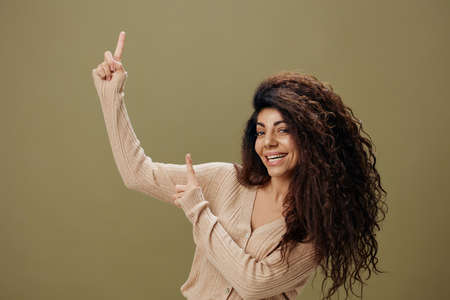 HEY LOOK HERE CONCEPT. Enjoyed cheerful tanned curly Latin female in casual things point fingers up...