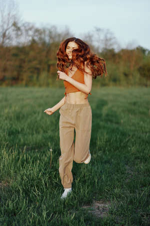 A woman works out and runs through the field in the park with a smile in a good mood looking at the...