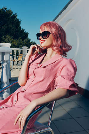 beautiful woman in pink dress sitting on a chair outdoors summer fashionの写真素材