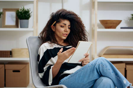 Concentrated pensive pretty beautiful curly tanned Latin woman with pen in hair in striped shirt...
