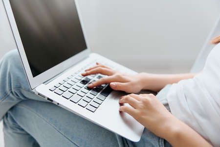 Side view of tanned lovely young Asian woman type message loads NFT project using laptop at interior...