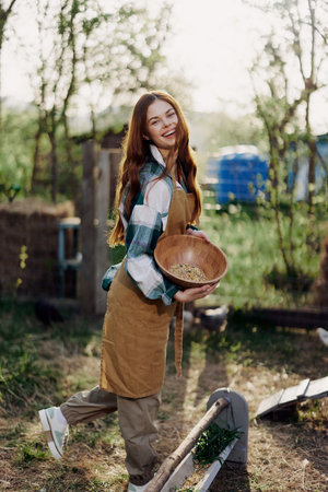 A young woman works on a farm and pours fresh feed from a bowl to feed the chickens and makes sure the food is clean and organic for the health of the faces and chickensの写真素材