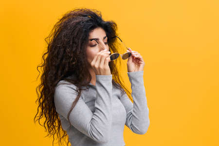COOL OFFER. Serious millennial pretty Latin female with afro wearing sunglasses with closed eyes, stay isolated over yellow background. Copy space, free place, fashion bannerの写真素材