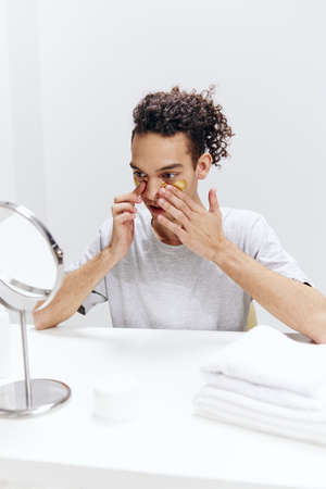 A young man in a white T-shirt sits at a table with a mirror and a towel face patches skin careの写真素材