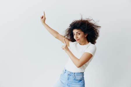 SEASONAL SUMMER SALE OFFER CONCEPT. Enjoyed pretty Latin female with waving afro hair smiling, look at camera, show copy free space. Cool offer for ad. Studio shoot isolated white backgroundの写真素材