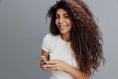 People And Technology Concept. Portrait of happy smiling young latin woman using smartphone standing...