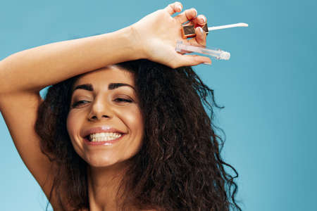 Cheerful sexy attractive curly Latin lady hold lip gloss overhead smile look aside posing isolated...