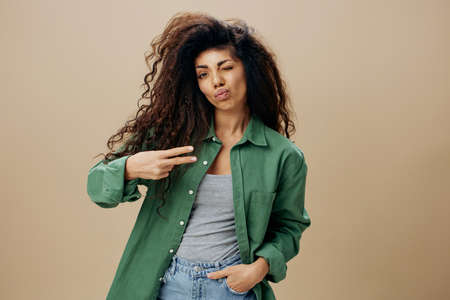Pretty enjoyed happy tanned curly Latin female in casual things wink gesture peace by fingers posing...