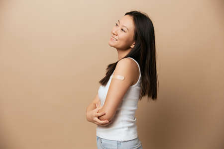 Portrait of cheerful cute tanned adorable young Asian lady after vaccination smiling posing isolated...