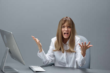 Irritated blonde businesswoman made a critical mistake using desktop computer spread hands sitting...