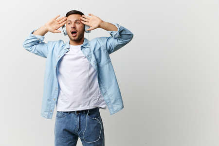 Excited shocked happy tanned handsome man in casual basic t-shirt headphones hold palms up listen cool music posing isolated on over white studio background. Copy space Banner Mockup. Playlist conceptの写真素材