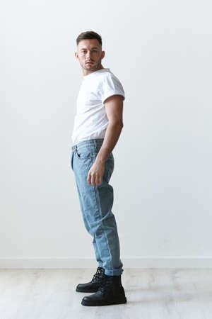 Full body side of view shot of handsome serious tanned serious man guy in basic t-shirt looks at...