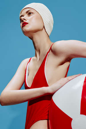 A woman swimmer in a bathing cap in a red swimsuit with a striped ball looks to the sideの写真素材