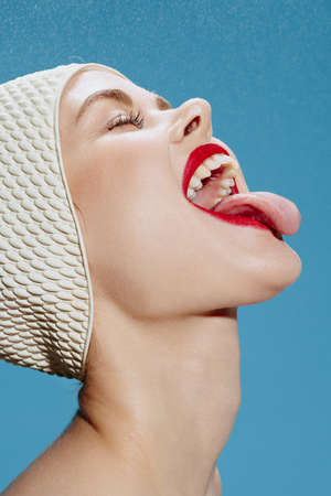 Funny cute girl in a swimming cap catches the rain from above with her tongue with her mouth open...