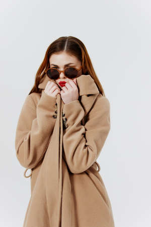 Advertising catalog shooting for the magazine. A red-haired stylish girl in a coat and glasses poses in the studio on a white backgroundの写真素材