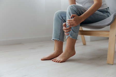 Closeup shot of pain leg calf suffering tanned beautiful young Asian woman touch ankle at home interior living room. Injuries Poor health Illness concept. Cool offer Bannerの写真素材