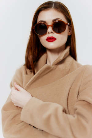 An elegant young woman in glasses and a coat poses for a clothing catalog on a white background. Concept Fashionの写真素材