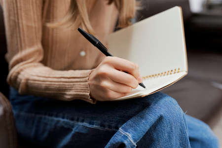 Closeup shot of hand blonde student lady with copybook sitting in sofa couch at modern living room...