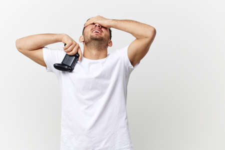 Tired frustrated sad tanned handsome man in basic t-shirt lose game session touch face with joystick gamepad posing isolated on white studio background. Copy space Banner Mockup. Gamer RPG conceptの写真素材