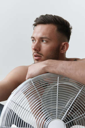 Modelling snapshots. Closeup portrait of attractive naked handsome man in jeans leaning on blower sitting on floor posing in white studio background. Fashion Men Shoot concept. Copy space. Cool offerの写真素材