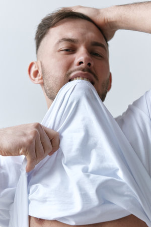 Portrait shot of handsome sexy flirting tanned man guy biting basic t-shirt touch hair posing on white background. Fashion Style New Collection Offer. Copy space for ad. Model snapの写真素材