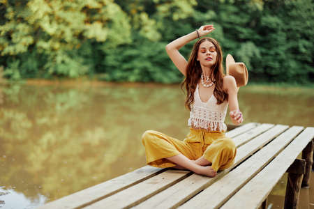 A young hippie woman sits on a lake bridge wearing stylish eco clothes and smilingの写真素材