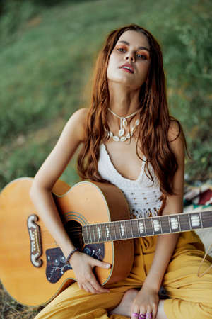 Happy hippie woman with a guitar smiles sitting in nature by the lakeの写真素材