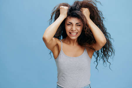 PROBLEMS CONCEPT. Crazy beautiful Latin female with afro rips out hair, have big troubles. Fashion. Studio shoot over blue sky background. Copy space, free place for design adの写真素材