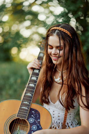 Happy hippie woman with a guitar relaxing in nature sitting on a plaid smiling and enjoying the...