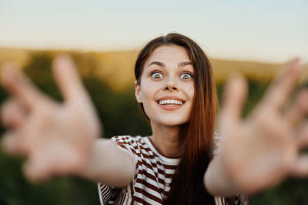 A woman smiles and pulls her hands to the camera close-up in nature with a view of the mountains. Happy travel lifestyle follow meの写真素材