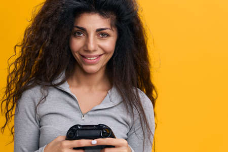 GAME OFFER. Photo portrait of attractive Latin female happy keeping joystick playing video game, holding trendy gamepad, isolated on orange yellow color background. Copy spaceの写真素材