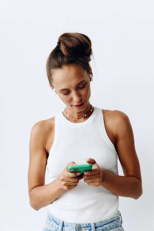 Young millennial woman listening to music on wireless headphones through her phone and smiling at...
