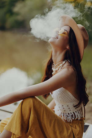 Young woman smokes wei in nature in a hippie way taking a break from the cityの写真素材
